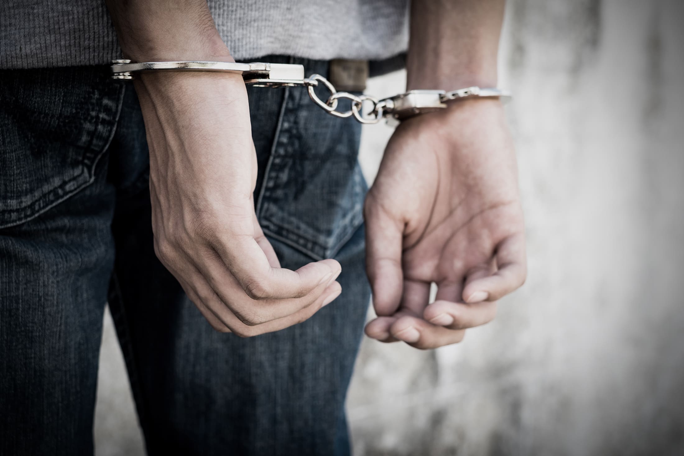 Close up hands tied up handcuffs in behind his body. Arrested man handcuffed hands at the back.